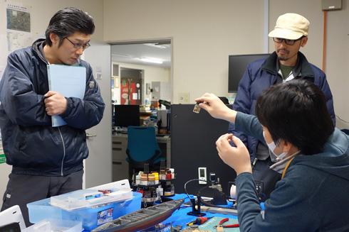 プラモデルを手にして話す社長と話を聞く社員2名