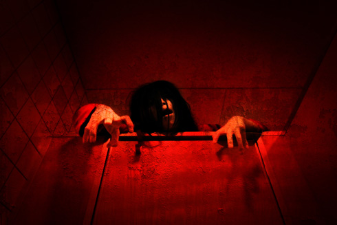 全体に赤みを帯びたトイレのうえから幽霊が顔を出している写真