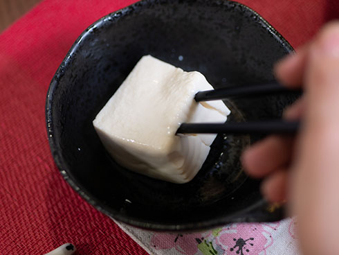 四角い湯豆腐を箸ですくうところ