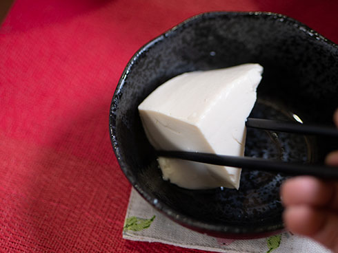 三角の湯豆腐を箸ですくうところ