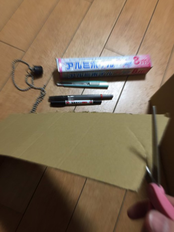 ダンボール、アルミホイル、マジックとハサミを持つ人