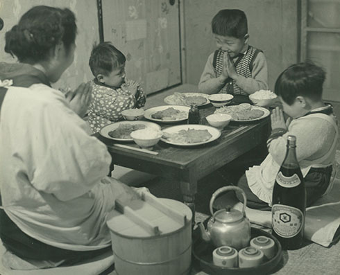 食卓を囲む家族　手前にラベルが見えるようにしょうゆ瓶が置かれている　みんなでいただきますポーズ