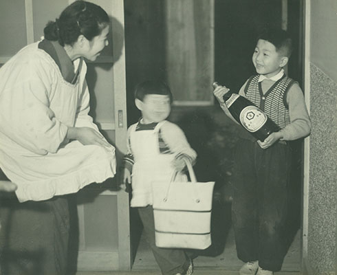 しょうゆ瓶を抱える少年と出迎える母