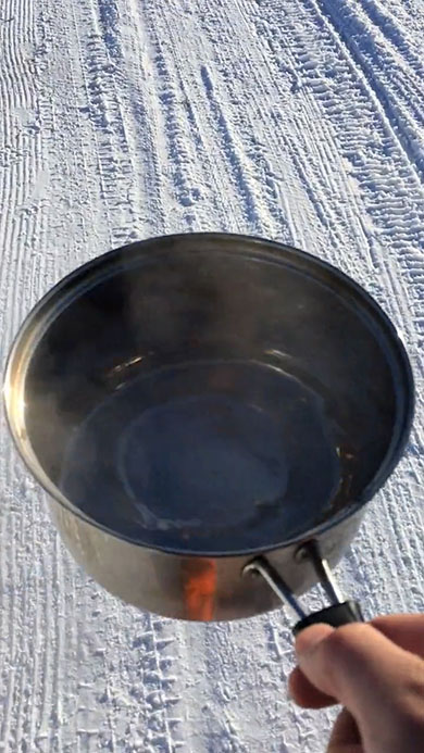 お湯を入れた鍋を持って雪の上を歩く様子