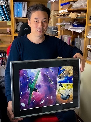 返礼品である直筆水彩画カラー原稿を掲げる須本壮一