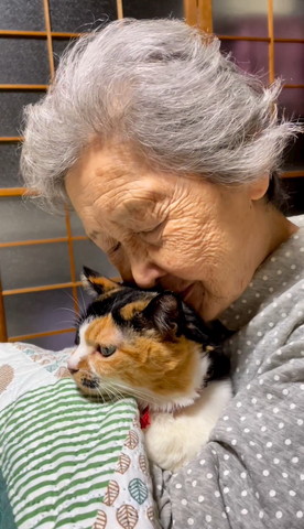 にっこりして猫の頭に顔寄せるおばあちゃん