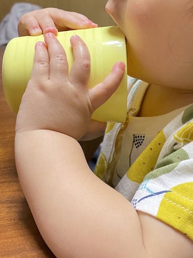 赤ちゃんがコップから麦茶をこぼしている写真