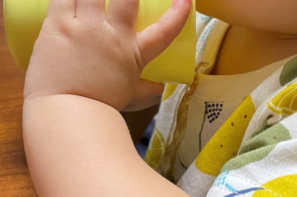 赤ちゃんがコップから麦茶をこぼしている写真