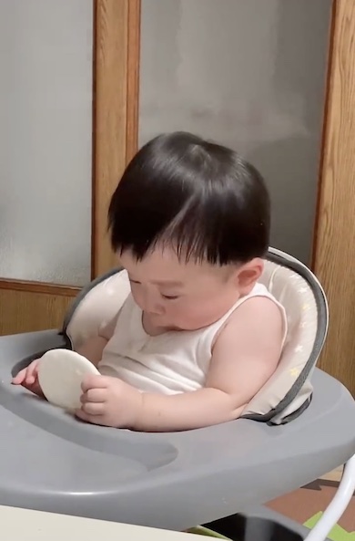 おせんべいを持ったまま眠気に襲われている赤ちゃんの写真1