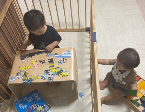 ベビーサークルの中で遊ぶお兄ちゃんと、外で遊ぶ赤ちゃんの画像