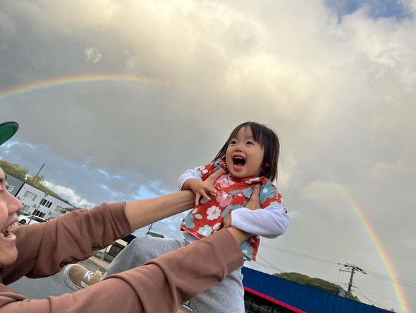 虹を背景にして高い高いをしてもらう2歳の女の子