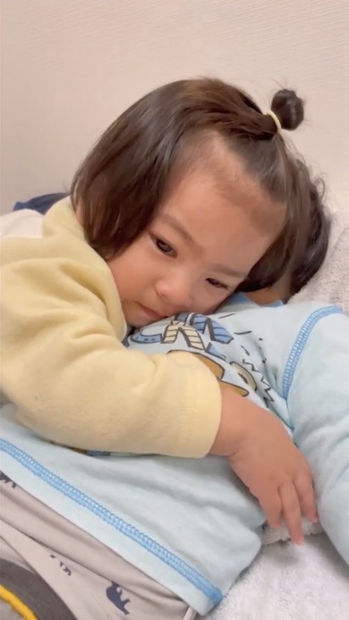 寝ている兄を抱きしめる1歳の女の子