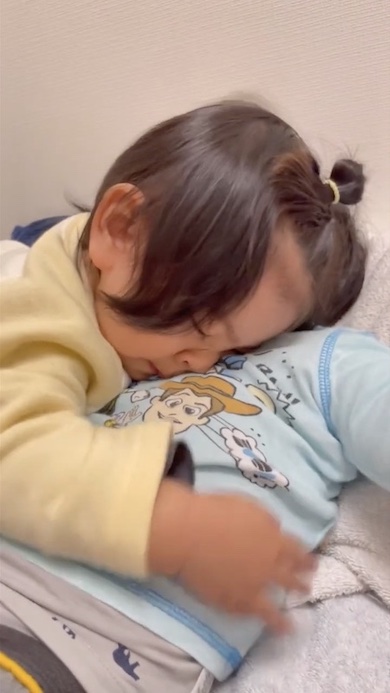 寝ている兄に顔をこすりつける1歳の女の子