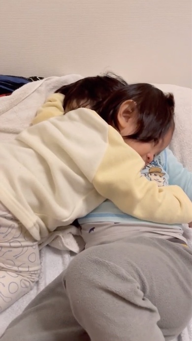 寝ている兄に抱きついている1歳の女の子