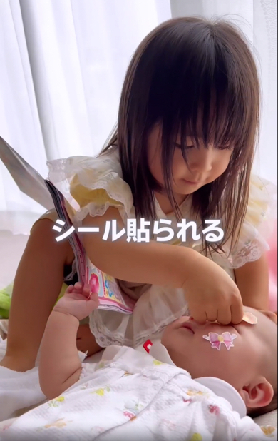 顔にシールを貼られる0歳妹