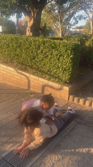 側溝で腹ばいになる兄を乗り越えていく妹