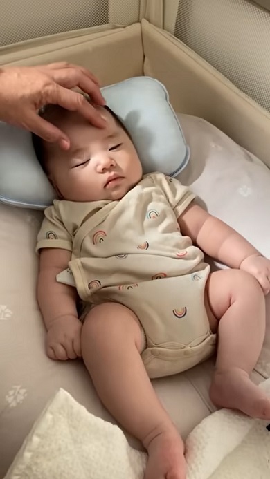 まゆ毛付近を押さえつけて赤ちゃんを寝かしつけようとする