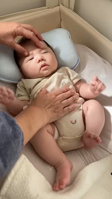 まゆ毛付近を押さえつけて赤ちゃんを寝かしつけようとする