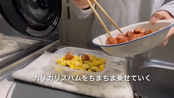刻み海苔と炒り玉子、焼いたサイコロ状のランチョンミートを乗せて「スパム丼」を作る様子