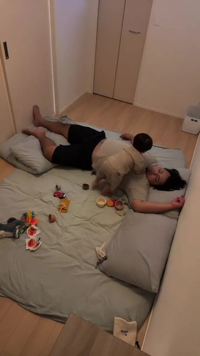 眠っているパパのそばで遊んでいる息子
