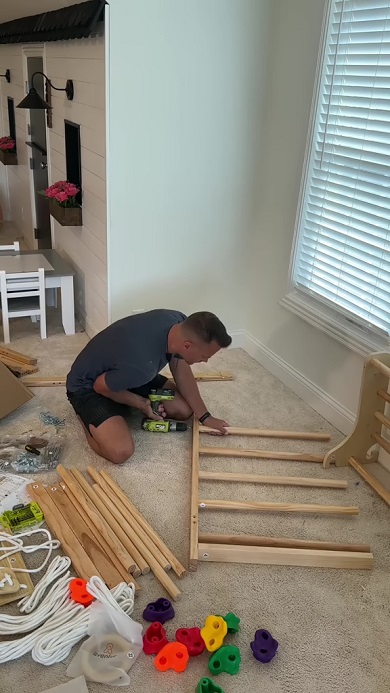 娘のために材料を組み上げて室内用の遊び場を作るパパ