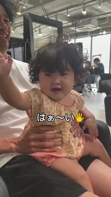 手を上げて前髪カットを了承するくるくるヘアな赤ちゃん