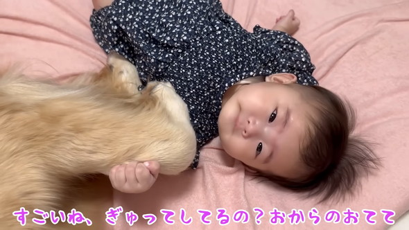 横になる赤ちゃんに寄り添うゴールデンレトリバーのワンコ