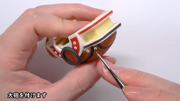 ピンセットでつまみながら粘土でできた大砲を取り付ける