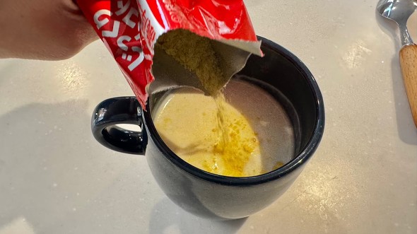 マグカップに入れてあたためた牛乳に、コーンポタージュの粉を入れている場面