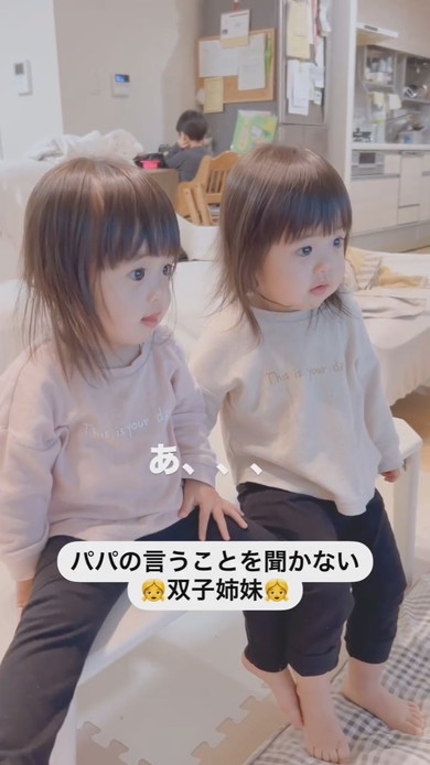 テーブルに座って注意される1歳の双子姉妹