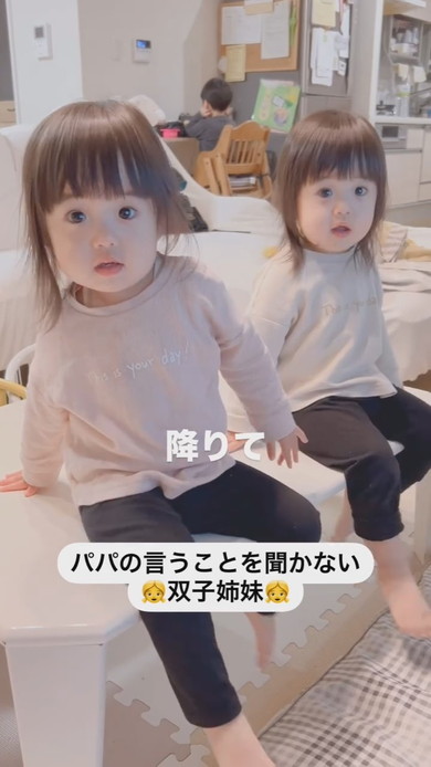 テーブルに座って注意される1歳の双子姉妹
