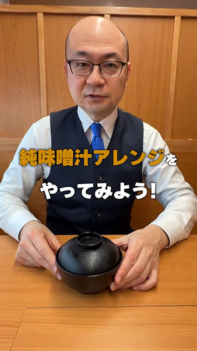 くら寿司公式YouTuberのイナバさんが純みそ汁を持っているところ。テロップに「純みそ汁アレンジやってみよう！」と書かれている