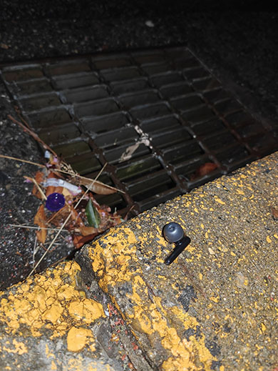 下水蓋の近くに黒いワイヤレスイヤフォンが落ちているところを写している