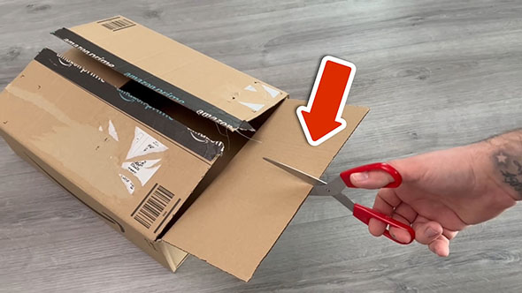 段ボールの内フラップの中心に切り込みを入れようとしているところ。ハサミの部分には赤い矢印が向いている
