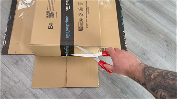 段ボールの底面を固定するテープにハサミを入れ、固定を解こうとしているところ