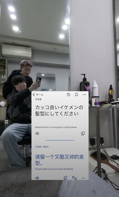 「カッコ良いイケメンの髪形にしてください」という日本語と、その中国語訳が表示されている。背景には男性が美容師に注文している様子が写っている。