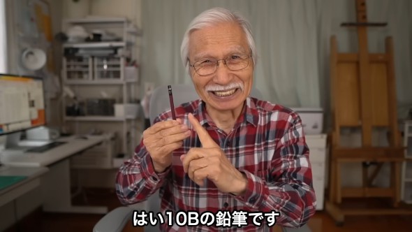 笑顔で10Bの鉛筆を紹介する白髪の男性。背景には画材や本棚がある作業部屋。「はい10Bの鉛筆です」という字幕付き。