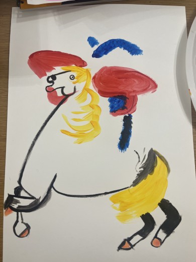 白い紙に描かれた馬のイラスト。黄色いたてがみとしっぽ、赤い耳と頬、青い絵の具で塗られた背景のアクセントが追加されている。