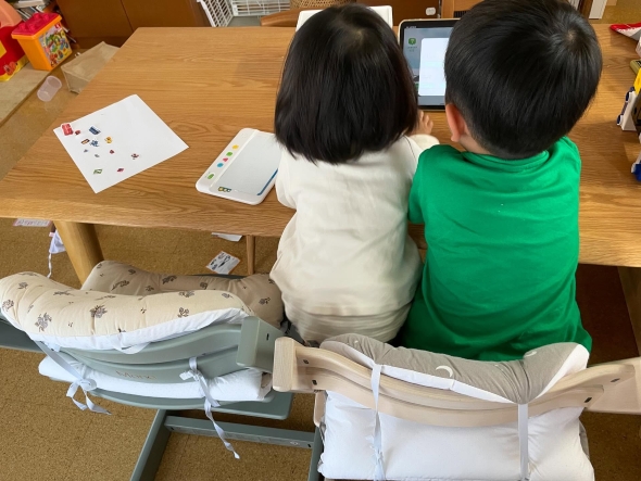 1つの椅子に座る兄妹の画像