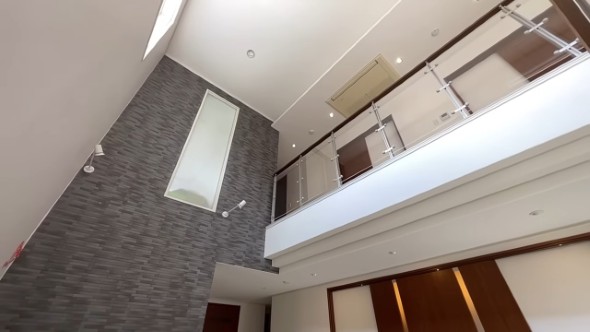 吹き抜けのエントランス空間。ダークグレーの石壁と縦長の窓、2階の廊下にはガラスと木材を組み合わせた手すりが設置されている。天井には埋め込み型のエアコン。