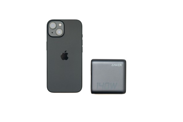 Anker 140W充電器と黒いiPhoneが並べて置かれ、サイズ比較がされている。白背景。