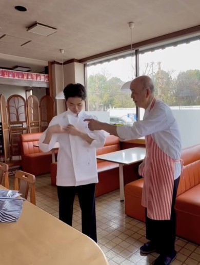 男性が白衣を着ながら、年配の男性から指導を受けているレストランの店内シーン。