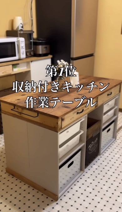 「第1位 収納付きキッチン作業テーブル」と書かれた画像。木製天板と引き出しが特徴の大型作業台で、下部には白い収納ボックスが並んでいる。